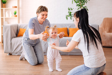 a little girl takes her first steps with the help of her parents. lesbians. The concept of a happy family.