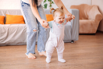 a little girl takes her first steps at home with her mother. the concept of a happy family