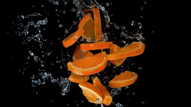 Super slow motion shot of rotating exploded orange slices with splashing water on black at 1000fps.