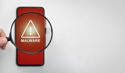 Magnifying glass on cell phone, an alarm sign detecting malware. Virus malware under magnifying...