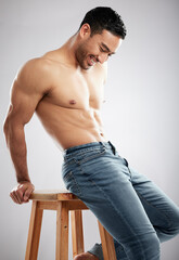 Laughing his way to the good life. Studio shot of a handsome young man showing off his muscular body while sitting on a chair against a grey background.