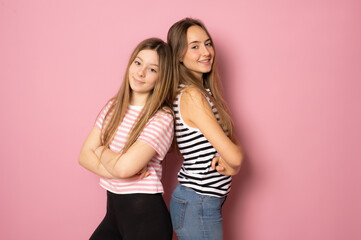 Portrait of two cheerful young women standing together and looking at camera isolated over pink background