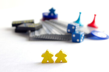 two yellow wooden meeple game pieces in front of blurry game parts
