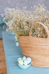 Wicker basket full of blooming branches of white gypsophila with easter eggs nearby.