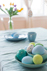 Close-up decorated Easter eggs in a plate on a table with a blue tablecloth.