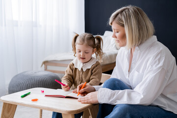 blonde woman and girl with ponytails drawing with colorful felt pens at home.