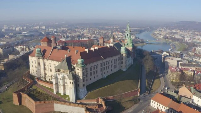 Drone camera camera moves from bottom to top of castle on Wawel hill, panoramic view of busy urban city Krakow Poland in morning fog. Aerial video footage. beautiful river Visla and Grunwaldzki bridge
