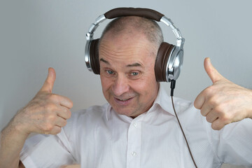 close-up of mature charismatic man 60 years in headphones listening to music with emotions on face gestures, on light gray background, concept learning foreign languages, live streaming and vlogging