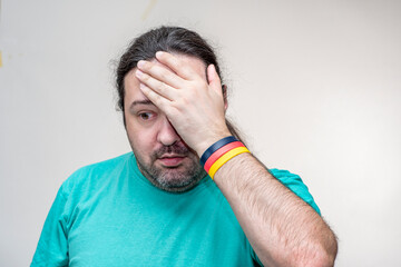 An adult, unshaven man in desperation holds his head. Bracelet in the colors of the German flag.