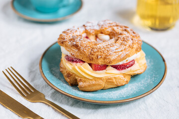 Traditional French Dessert called Paris Brest on a light grey background with powder sugar and strawberries
