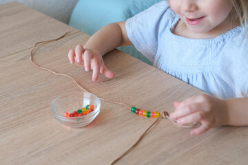 small child, toddler stringing colored plastic beads on string, kid's fingers close-up, concept of...