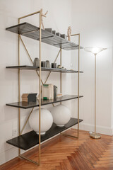 Decorative gold metal shelf and black wooden shelves on oak parquet floors and matching lamp