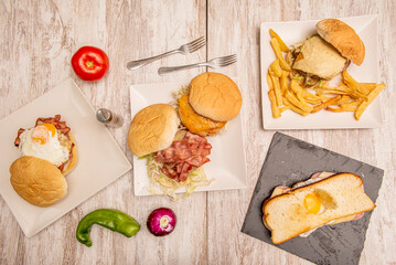 Fast food dishes with assorted burgers, homemade french fries, sandwich with fried egg and tomatoes and peppers on the pickled wooden table