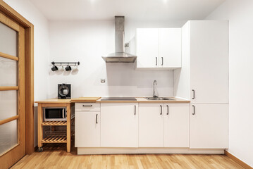 Kitchen front with combined furniture with wooden countertop and white furniture with integrated appliances and oak wood floors