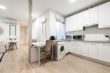 Open kitchen with white wood cabinets with gray top and access to a room with light furniture, white dining table, oak wood flooring
