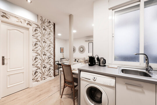 Cocina abierta con gabinetes de madera con sobre gris y acceso a una sala con muebles claros y empapelado en las paredes