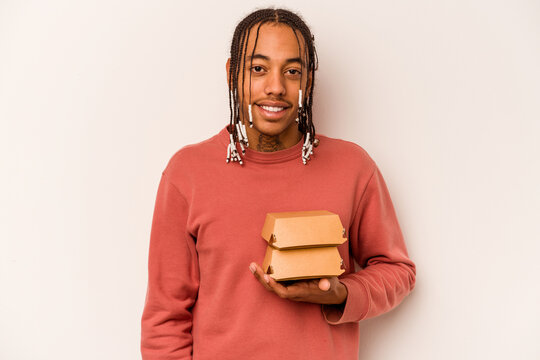 Young African American Man Holding A Burger Isolated On White Background Laughing And Having Fun.