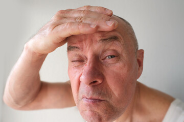 close-up charismatic mature man 60 years old looks in mirror at his reflection, critically examines...