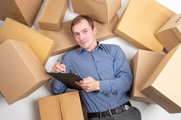 Courier job. Man is lying on the floor in the middle of cardboard boxes. Delivery man with...