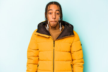 Young African American man isolated on blue background shrugs shoulders and open eyes confused.