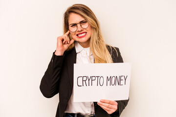 Young business caucasian woman holding a crypto money placard isolated on white background covering ears with hands.