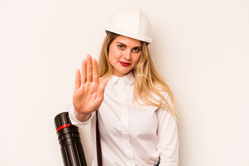 Young architect woman with helmet and holding blueprints isolated on white background standing with outstretched hand showing stop sign, preventing you.