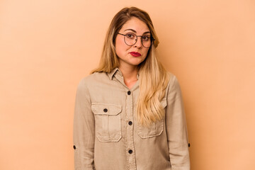 Young caucasian woman isolated on beige background shrugs shoulders and open eyes confused.
