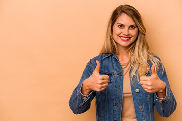 Young caucasian woman isolated on beige background smiling and raising thumb up