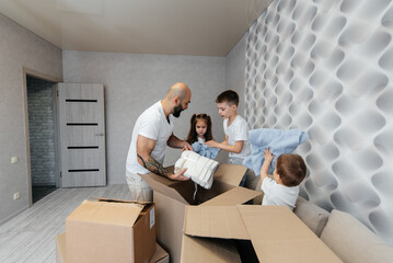 A young father with children unpacks a box of things after moving to a new apartment. Purchase of real estate. Housewarming, delivery and transportation of goods.