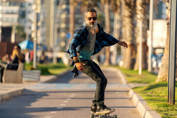 latin beard senior man skateboard on bikeway and having fun in La Serena
