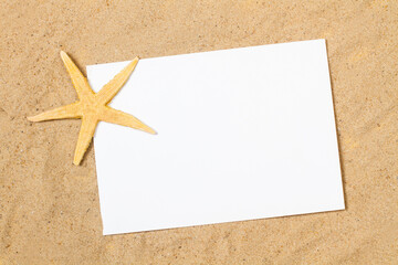 Estrella de mar junto a un papel en blanco sobre un fondo de arena. Vista superior y de cerca. Concepto: Turismo, viaje, espacio publicitario