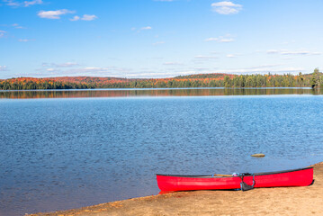 Empty red canoe on a sandy beach on a beutiful lake with forested shores on a clear autumn day