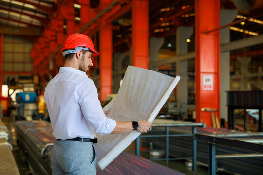 Back View, Behind, Rear. Portrait Of Architect And Civil Engineering Builder Holding Layout Plan On Factory Under Construction Site.