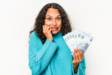 Young hispanic woman holding banknotes isolated on white background biting fingernails, nervous and very anxious.