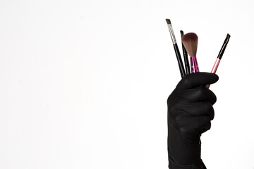 Professional makeup brushes, A hand in a black glove holds a set of professional makeup brushes on a white background. place for text. Makeup, Brushes.