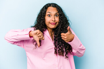 Young hispanic woman isolated on blue background showing thumbs up and thumbs down, difficult...