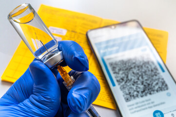Spritze mit Injektionsflasche vor Impfausweis in Papieform und digital auf dem Smartphone