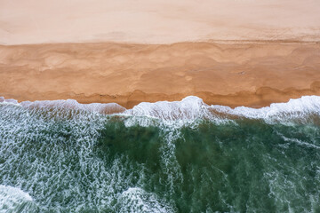 Naklejka na ściany i meble drone view of whitecapped waves crashing on an empty golden sand beach