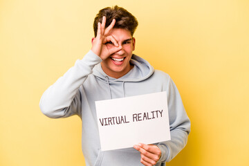 Young caucasian man holding virtual placard isolated on yellow background excited keeping ok gesture on eye.