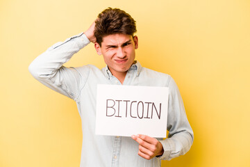 Young caucasian man holding bitcoin placard isolated on yellow background being shocked, she has remembered important meeting.