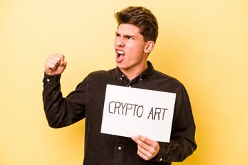 Young caucasian man holding crypto art placard isolated on yellow background raising fist after a victory, winner concept.