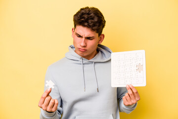 Young caucasian man holding puzzle isolated on yellow background