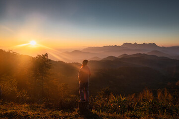 Asian female hiker standing and looking the sunrise on mountain peak in the morning at Doi Kham Fah national park