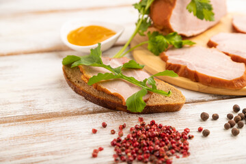 Smoked pork ham on cutting board on white wooden background. Side view, close up, selective focus.