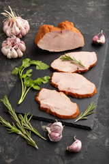 Smoked pork ham on cutting slate board on black concrete background. Side view, close up.