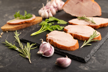 Smoked pork ham on cutting slate board on black concrete background. Side view, close up, selective focus.