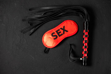 BDSM, bondage play, fetish wear and kinky sex toy concept with close up on erotic mask and red handcuffs isolated on black silk background - obrazy, fototapety, plakaty