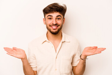 Young hispanic man isolated on white background makes scale with arms, feels happy and confident.