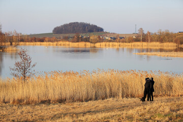 Para młodych ludzi z psem na spacerze brzegiem jeziora. 
