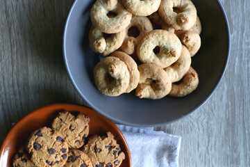 Plate of chocolate chip cookies and bowl of sugar cookies on wooden table. Flat lay.